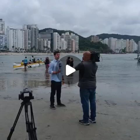 Repórter e cinegrafista gravando na praia das Astúrias, no Guarujá, durante o evento de surfe adaptado do Dia Internacional das Pessoas com Deficiência.